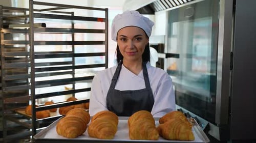 Smiling Baker Holding Freshly Baked Croissants in Kitchen