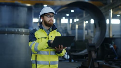 Industrial Engineer in Hard Hat Wearing Safety Jacket Uses Touchscreen Laptop and Walks. He Works a