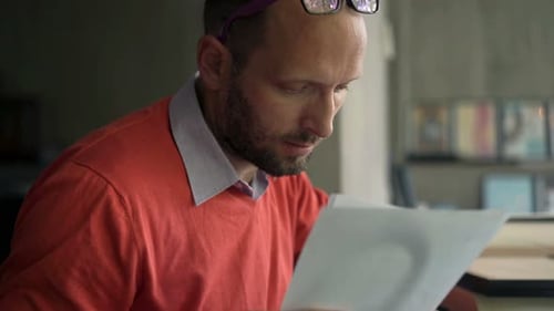 Man Reads Documents at Desk with Laptop