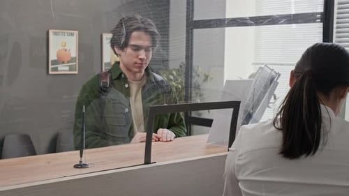 Customer Interacting with Bank Teller at Counter Separated by Transparent Screen