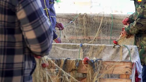 Close up of unrecognizable fishermen in port collecting fishing nets in slow motion