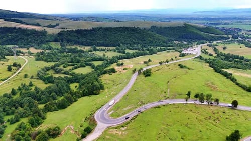 Cars ride by the wavy road crossing the valley with cow herd grazing on.