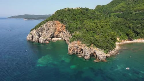 Beautiful top view of the transparent sea and rocky shore with forest. People swim and swim on SUP.