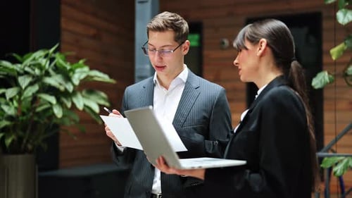 Businessman And Businesswoman Discuss Project Using Laptop In Modern Office