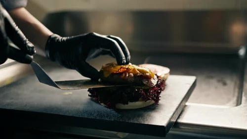 kitchen in restaurant chef puts burger patty with cheese on burger buns prepares dish for serving