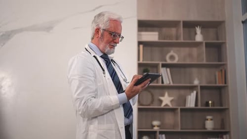 Mature Senior Male Doctor in Medical Uniform Using Digital Tablet in Clinic Therapist Professional