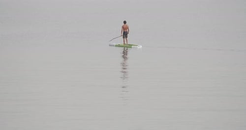 Young fit man moves effortless in a paddle board in calm sea at sunrise in slow motion 60fps