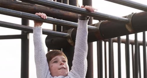 Fun and playful boy playing on monkey bars, jungle gym or playground in park