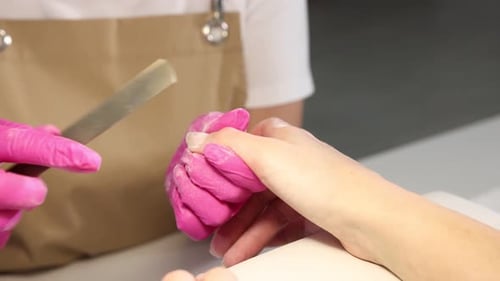 Professional manicurist filing client's nails in beauty salon, closeup