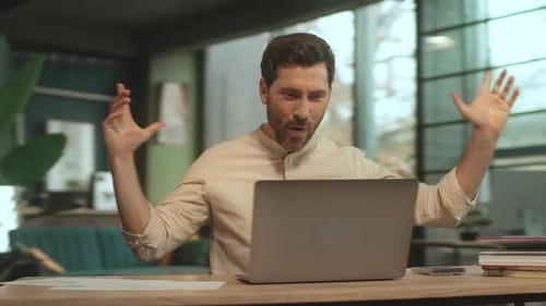 Excited Man Celebrates Success at Desk with Laptop