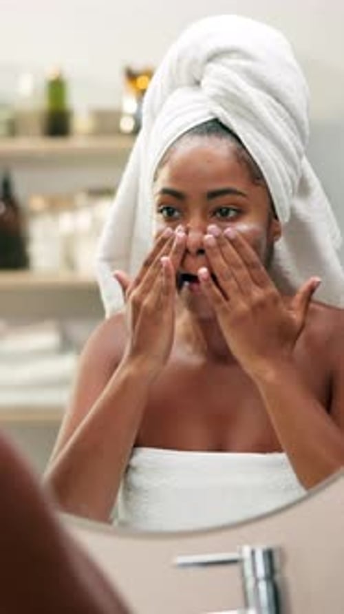 Woman Applying Cream to Face in Mirror