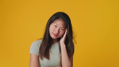 Young woman looking at camera, smiling and flirting isolated on yellow background in studio