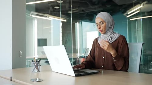 Muslim young businesswoman entrepreneur in hijab feels hot during computer work and turn on remote c