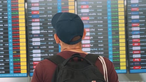 Man with Backpack Checking Flight Information on Digital Board at an Airport Preparing for His