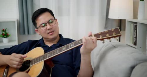 Man Playing Guitar on Sofa at Home