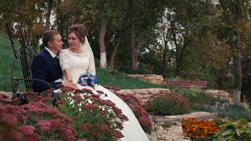 The Newlyweds are Sitting on a Bench in a Green Garden