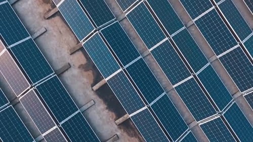 Flying over the solar farm with sunny reflection on panels.