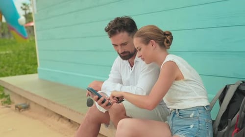 Couple Using Cellphone on Beach Bungalow Porch