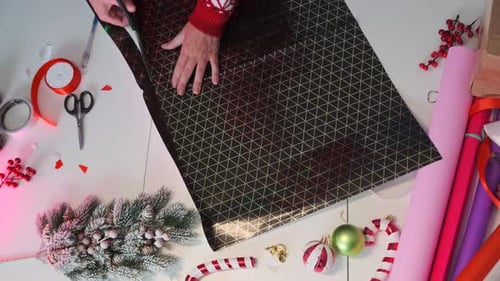 Female hands cutting wrapping paper to pack a holiday gift on a table during Christmas holiday.