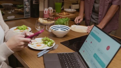 Couple Preparing Breakfast in Kitchen, Using Phone, Laptop