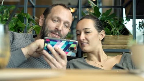 Young caucasian couple enjoying smartphone together in a cheerful cafe