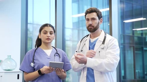 Portrait of two serious doctors man and woman standing in hospital clinic looking at camera.