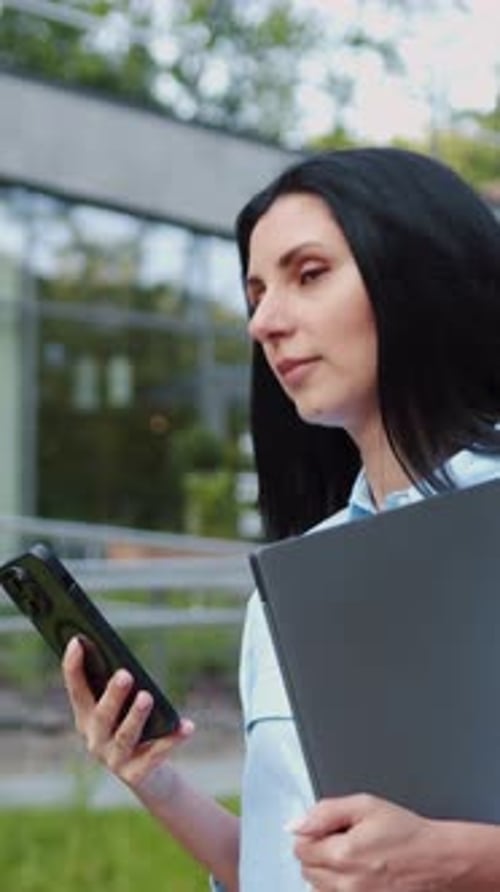 Portrait of Caucasian Woman with Dark Hair Using Mobile Phone with a Pleased Smile Standing in Front