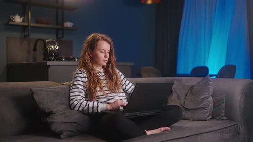 Young Freelancer Woman Working with Laptop From Home Sitting on Sofa in Living Room at Night Female