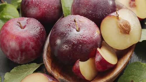 Ripe plums fruits with plum slices slowly move in the wooden bowl on a gray stone table