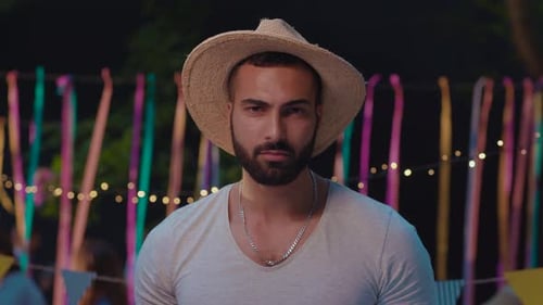 Smiling man wearing hat points towards camera at party