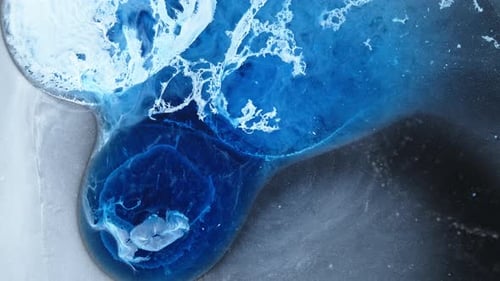 Close-up of ink mixing in water, showing vibrant blue liquid blending and swirling