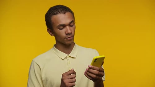 Young Adult Using Mobile Phone on Yellow Background