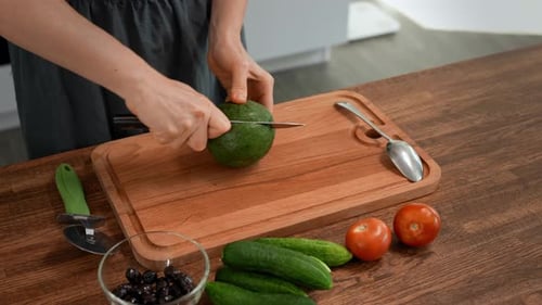 Woman Cutting an Avocado in Kitchen for Salad
