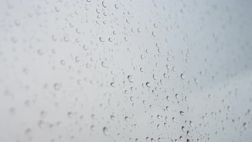 A close-up shot of heavy rain drops is seen through a window glass.
