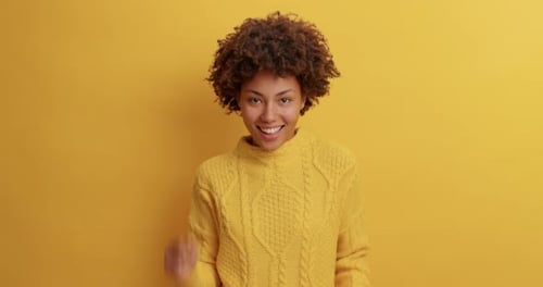 Smiling woman with afro dancing against yellow background