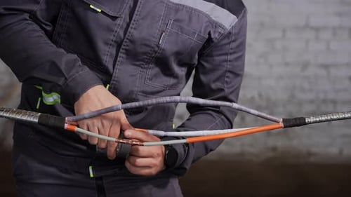 Un ouvrier qualifié joint méthodiquement des fils haute tension à l'aide de manchons de protection et méticuleusement