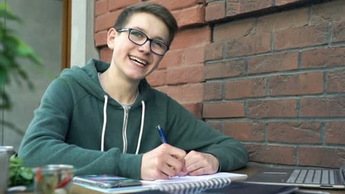 Cheerful teenage student smiling and studying homework in a coffee shop