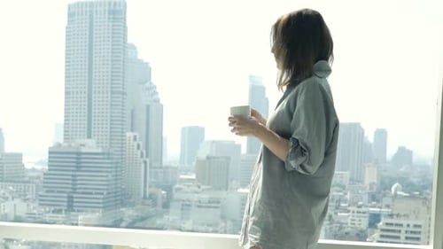 Young, Pretty Woman Drinking Coffee and Admire View From Window at Apartment 30s