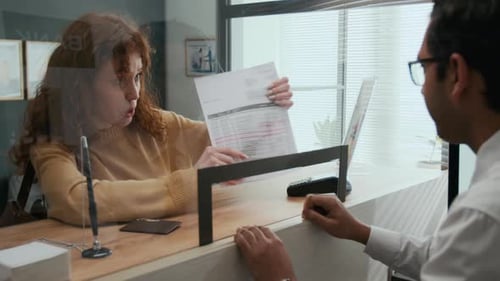 Angry Woman Addressing Issue and Showing Documents to Bank Teller in Office