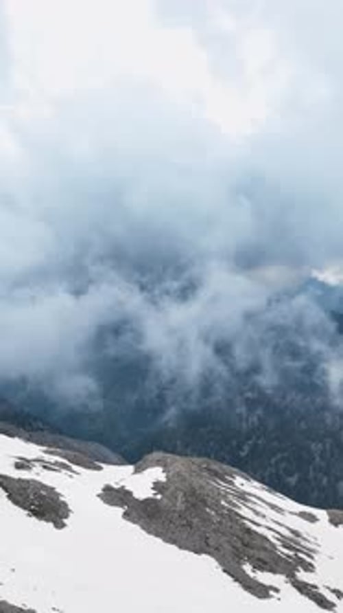Vidéo verticale : Nuages majestueux enveloppant les sommets enneigés, perspective aérienne de la nature