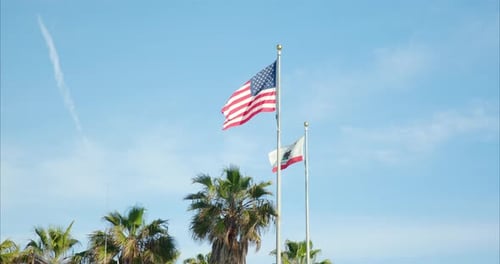 American and California Flags Waving Under Blue Sky