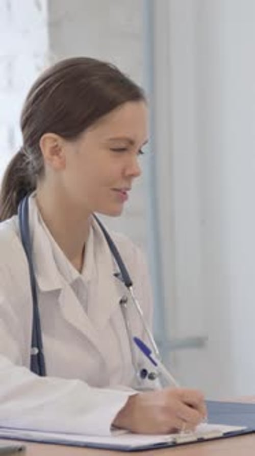 Woman Doctor Writing on Clipboard in Hospital Office
