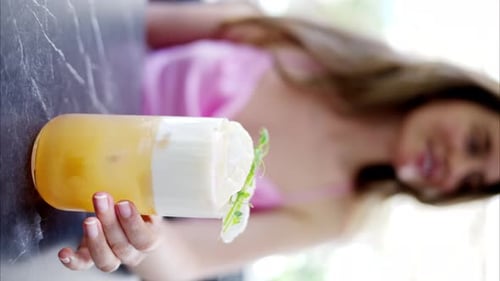 Woman holding a summer white and orange cocktail with whiskey and peach juice, slow motion vertical