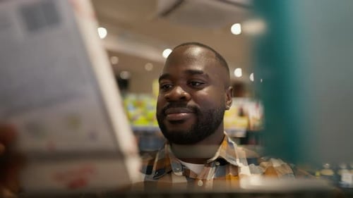 Closeup Shot of a Black Man Choosing One of Two Products on the Floor in a Supermarket