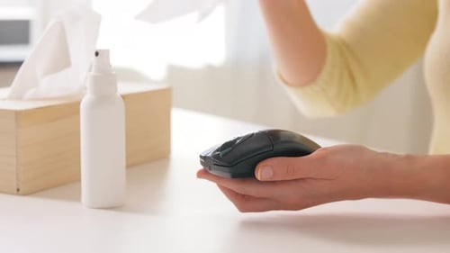 Woman Cleaning Computer Mouse With Sanitizer and Wipe
