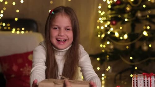 Smiling Kid Girl Receiving Christmas Gift Box From Parents in Decorated Room