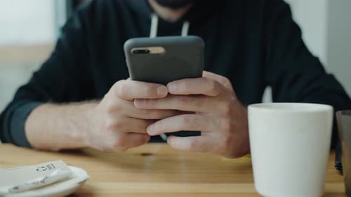 Man Using Smartphone at Cafe with Coffee Cup on Table