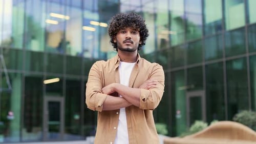 Portrait of a young adult businessman seriously looking at camera while standing on the street near