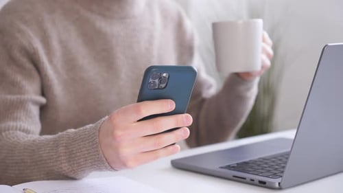 Woman Holding Phone and Coffee Mug at Desk