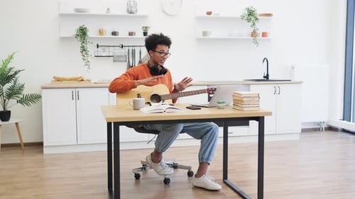 Young Man Plays Guitar During Online Lesson at Home